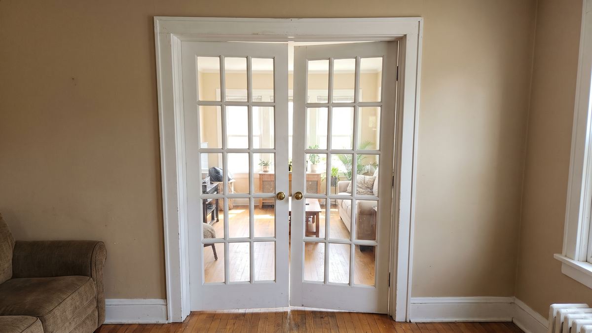 Pair of white French doors, the right door sagging on its hinges with a wedge-shaped gap, not closing