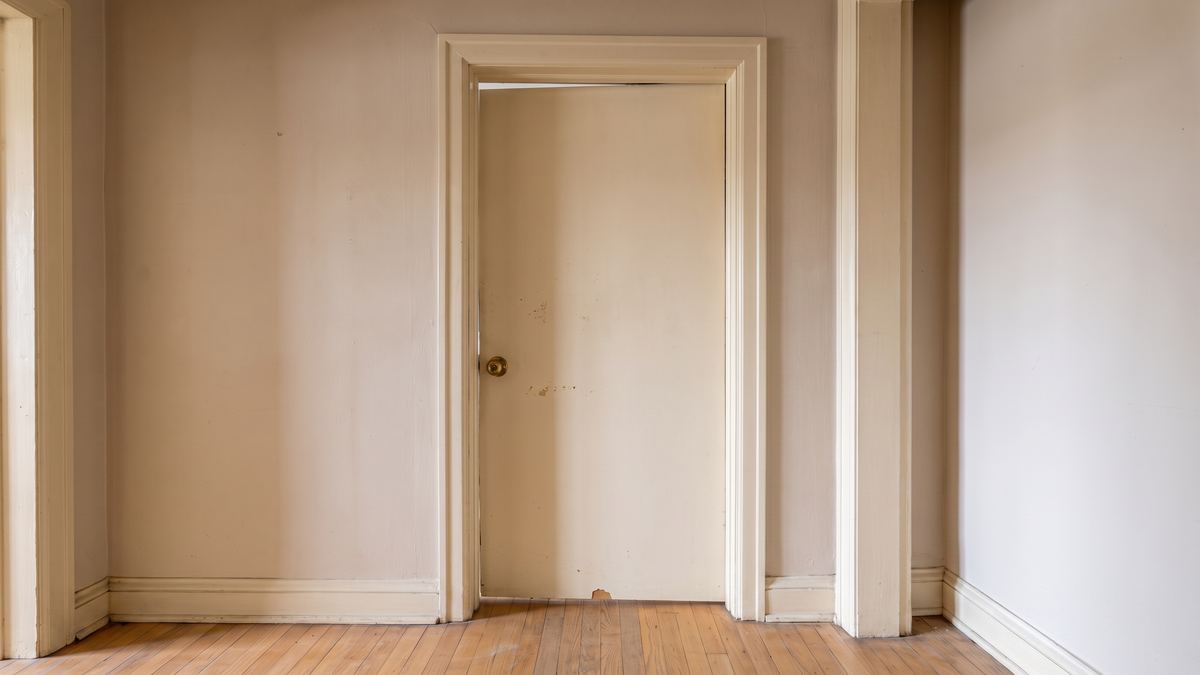 Dated 1980s hollow-core hallway door with an old brass knob, hanging slightly off in its opening