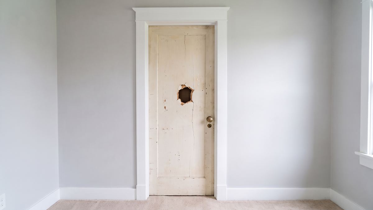 Old damaged hollow-core bedroom door with a punched hole and an old brass knob, the frame and casing around it sound