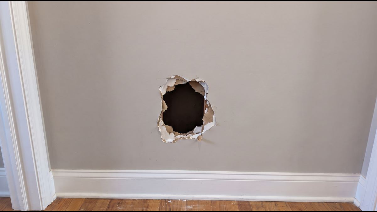 Jagged hole the size of a sheet of paper punched through a hallway wall