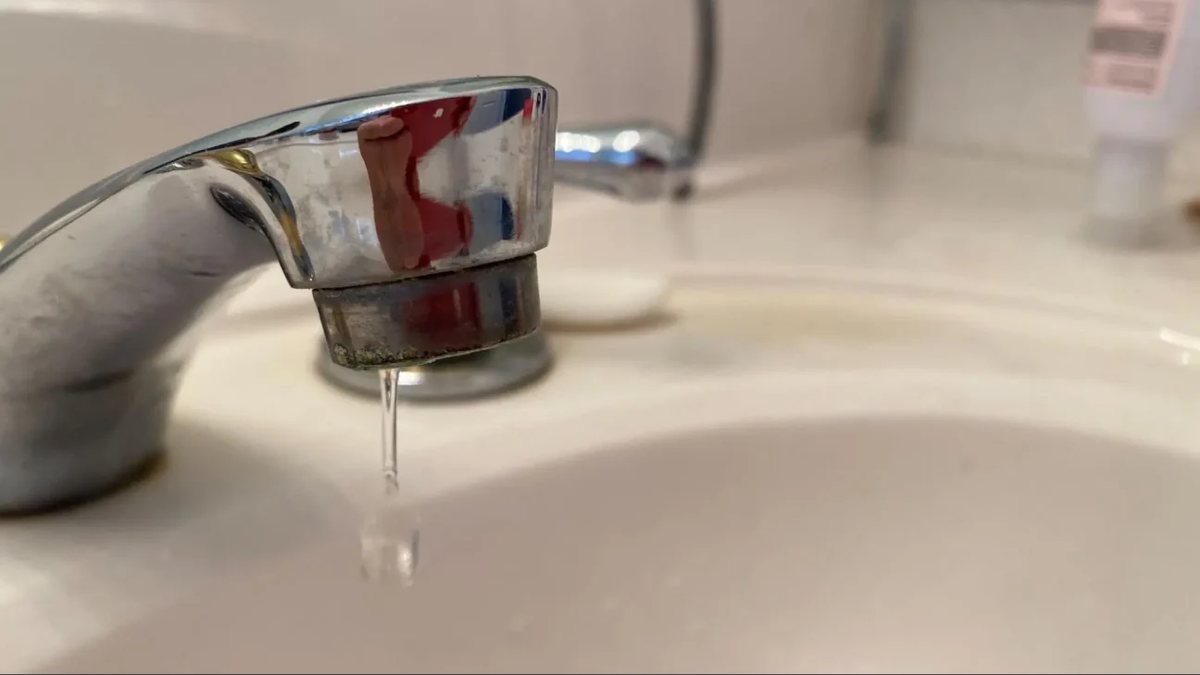 Old bathroom faucet with a corroded spout, dripping into a stained sink