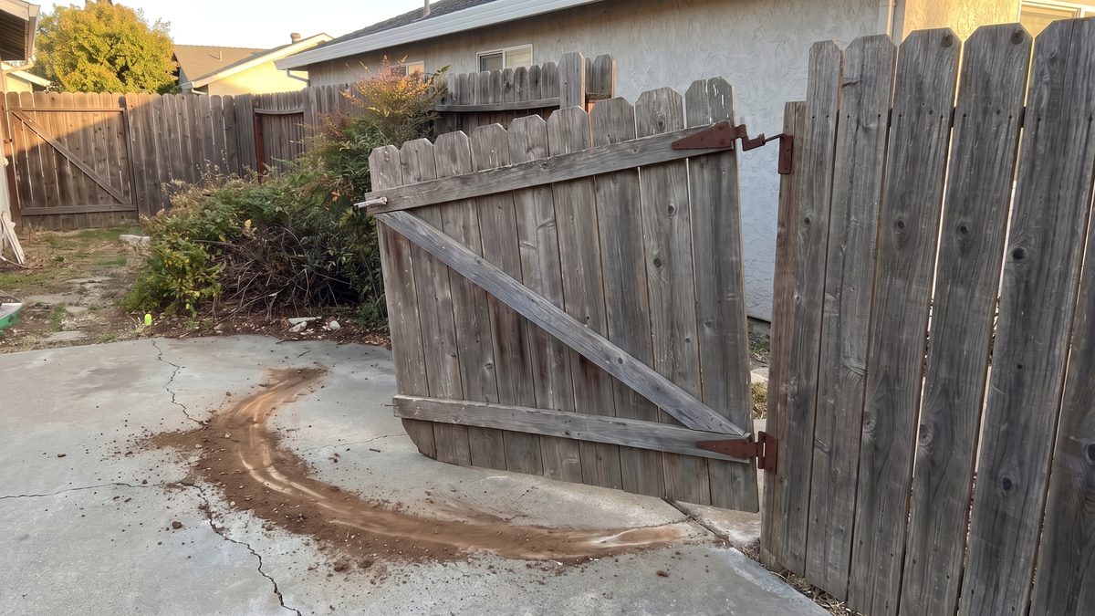 Gate dragging on the concrete, hanging off a rusted hinge, fence beside it sound
