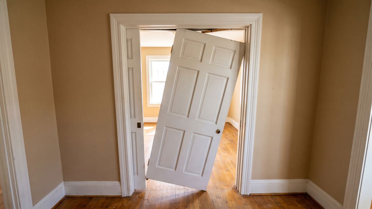White six-panel pocket door off its overhead track, hanging crooked in the opening