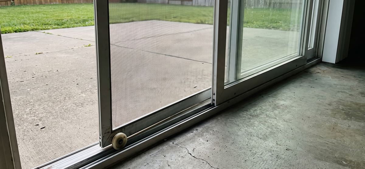 Sliding screen door jumped off its bottom track with the worn roller showing before repair in San Diego
