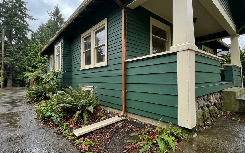After: the same bungalow with new cedar lap painted deep green and the soil and ferns pulled back from the wall