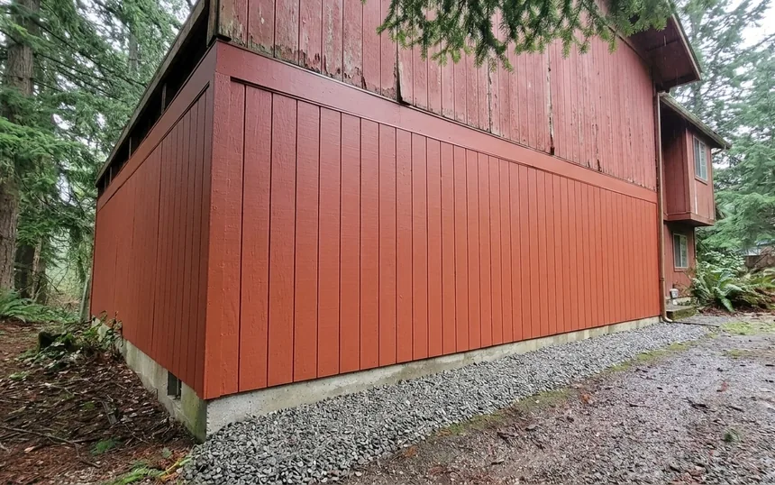 After: the same house with new T1-11 panels painted barn red and the needles cleared from the base