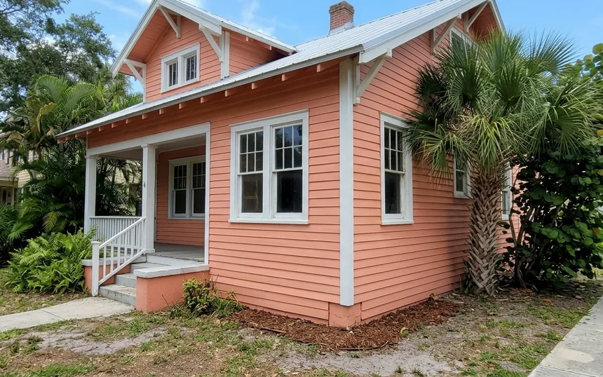After: the same house with new lap siding at the corner and under the window, primed and painted coral