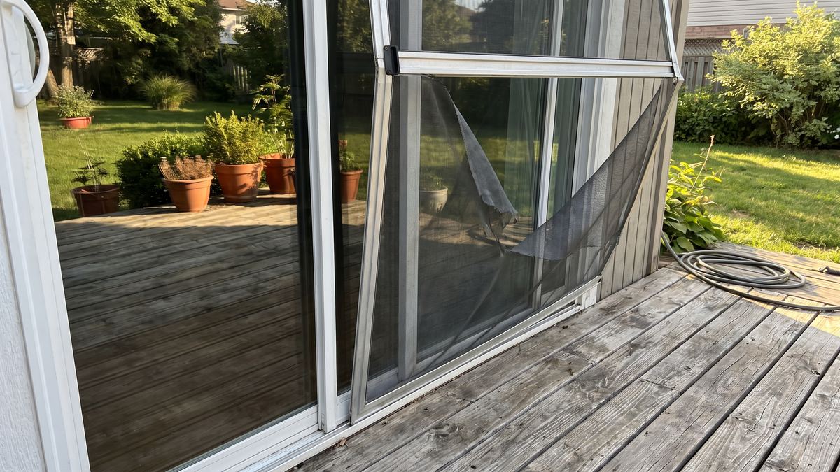 Torn sliding screen door off its rail beside a patio slider before repair in San Diego