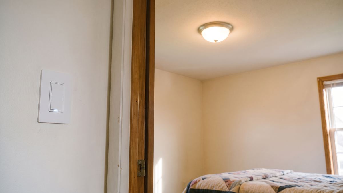 Same bedroom doorway with a smart light switch installed and the ceiling light on