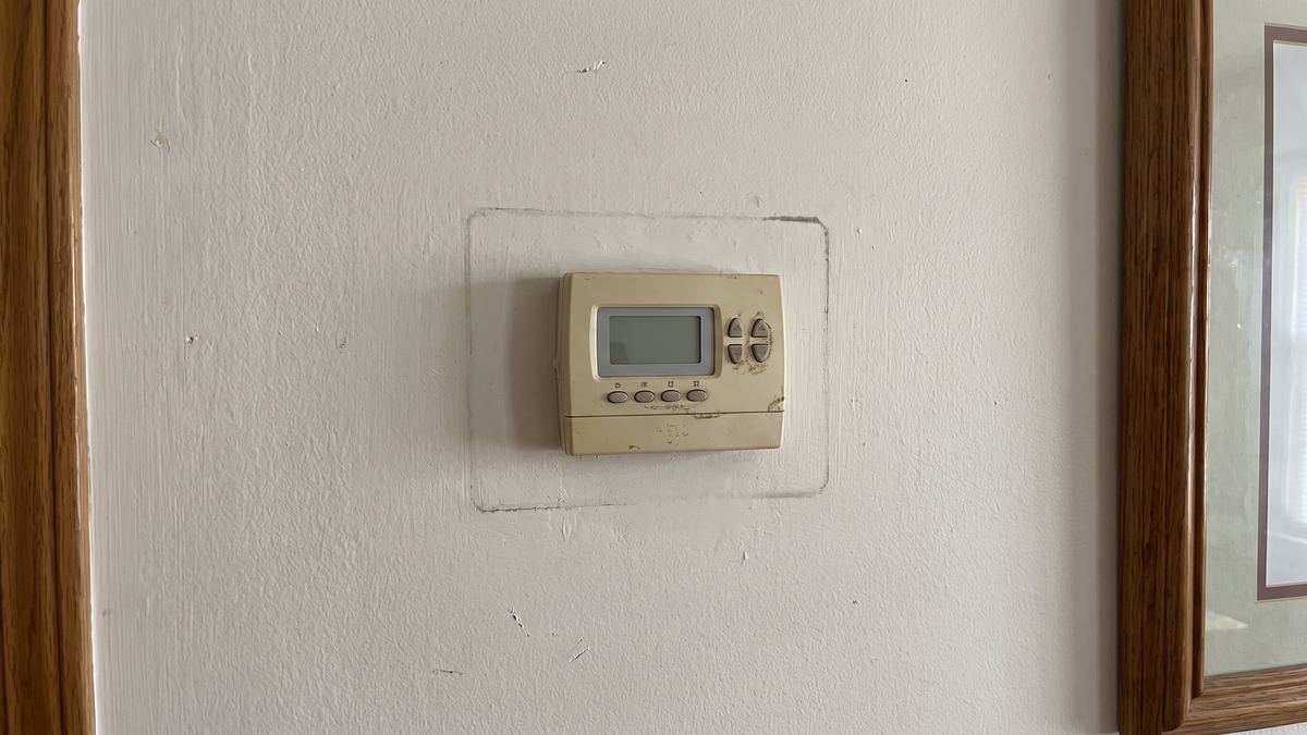 Old beige programmable thermostat on a wall beside a doorway