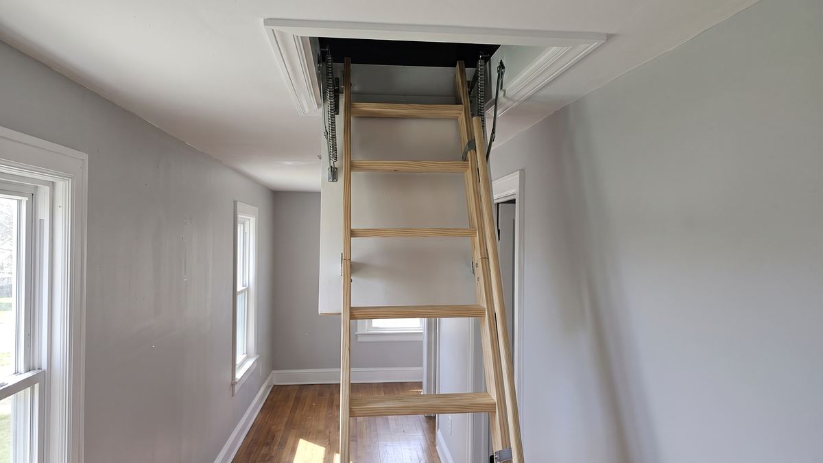 Same hallway with a new folding attic ladder installed and fresh trim around the opening