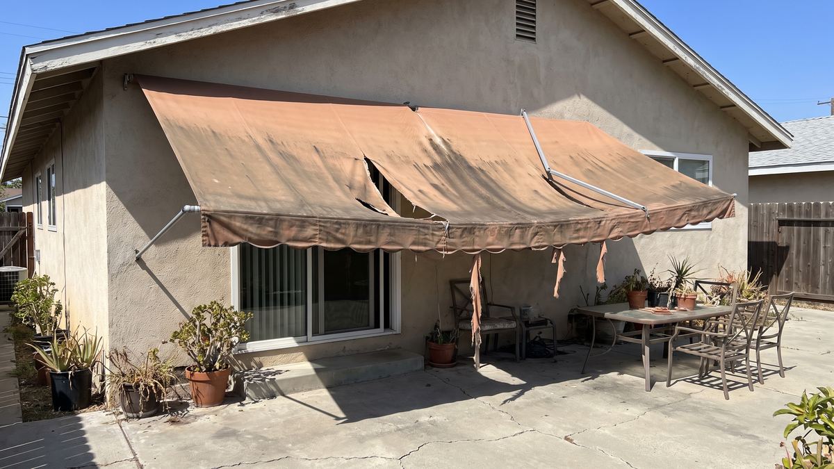 Back patio with a torn, faded fabric awning sagging over the sliding door