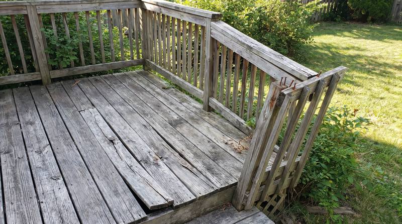 A weathered deck with cracked boards and a loose railing before repair