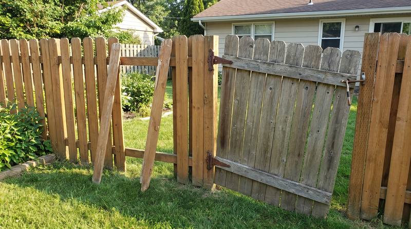 A wood fence with broken pickets and a sagging gate before repair