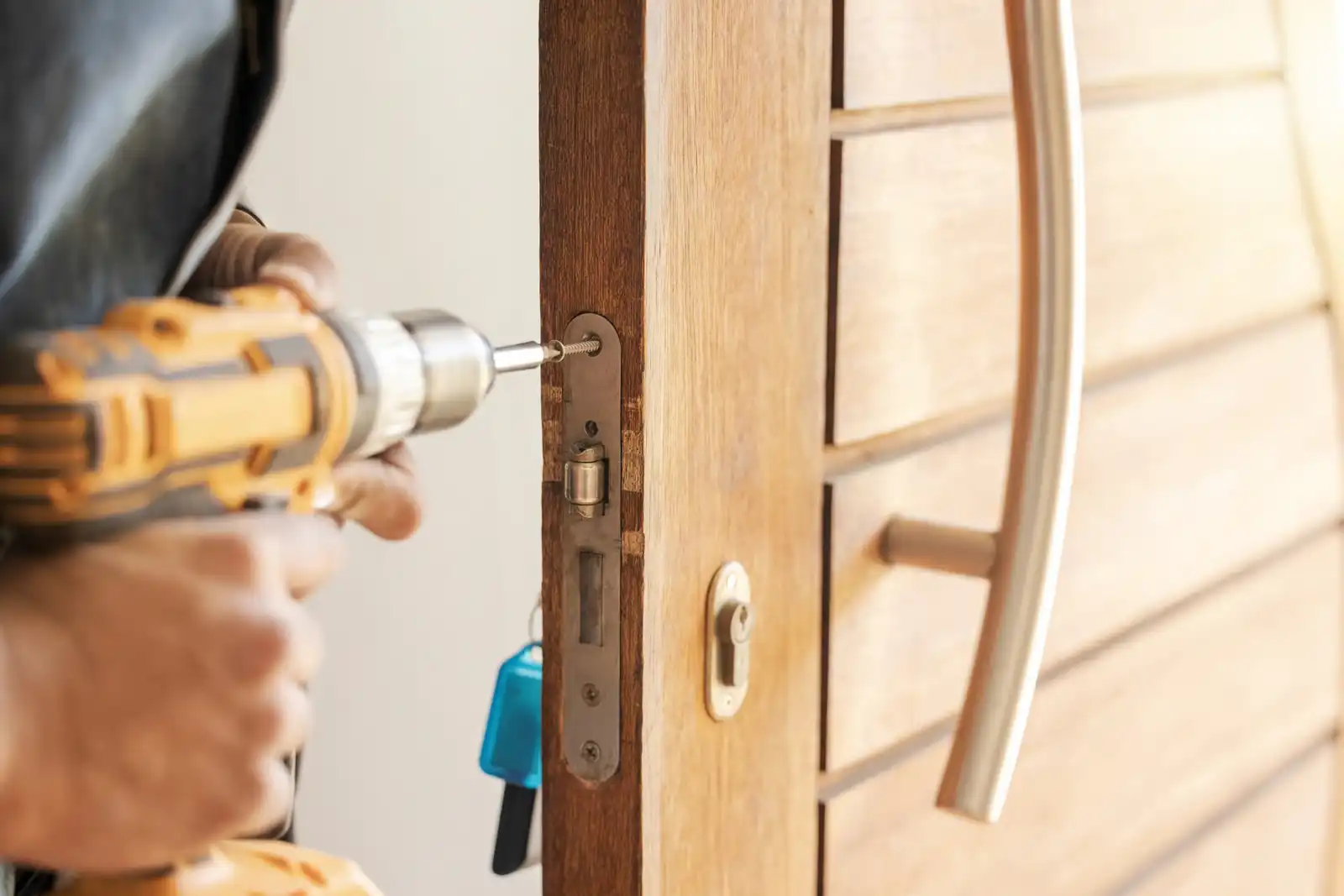 Technician installing a door lock with a power drill on a wooden front door