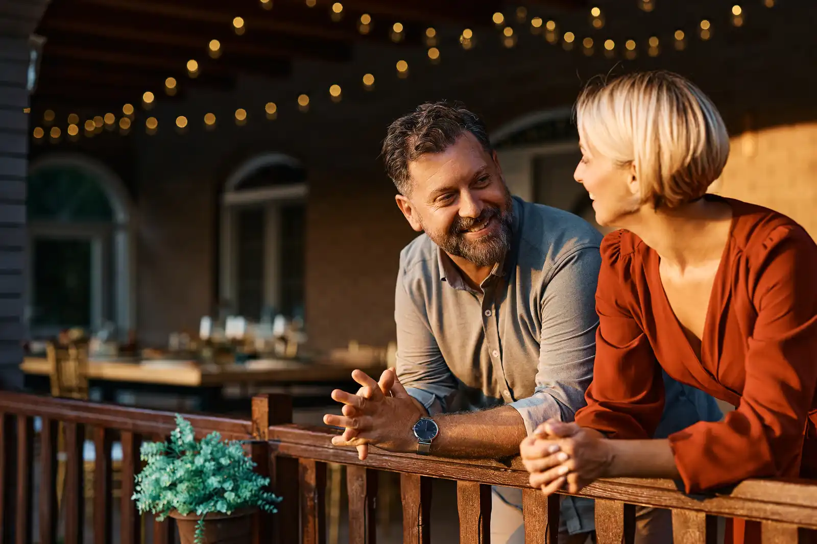 Couple relaxing on a deck railing under string lights at dusk