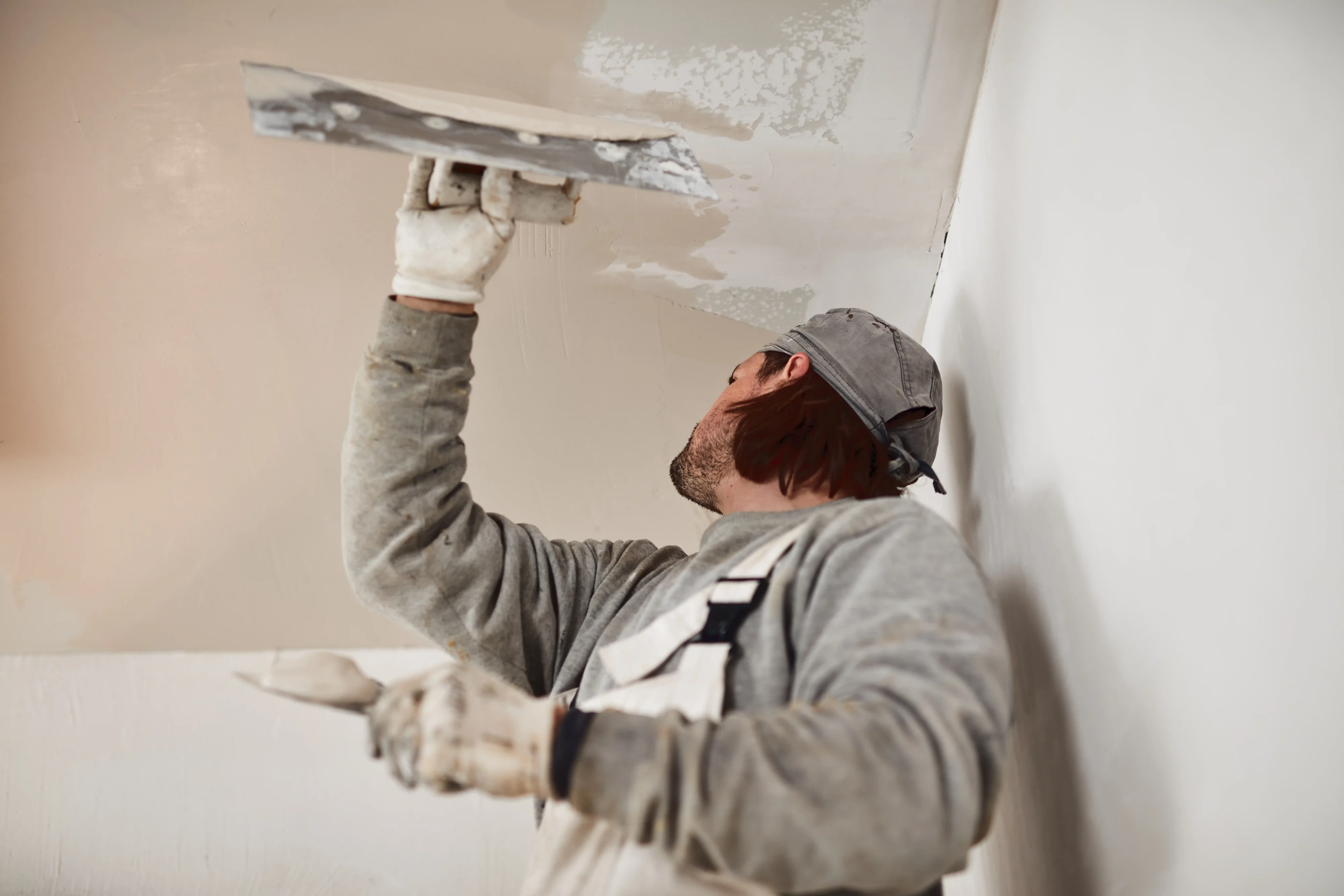 Professional worker plastering drywall wall with putty knife